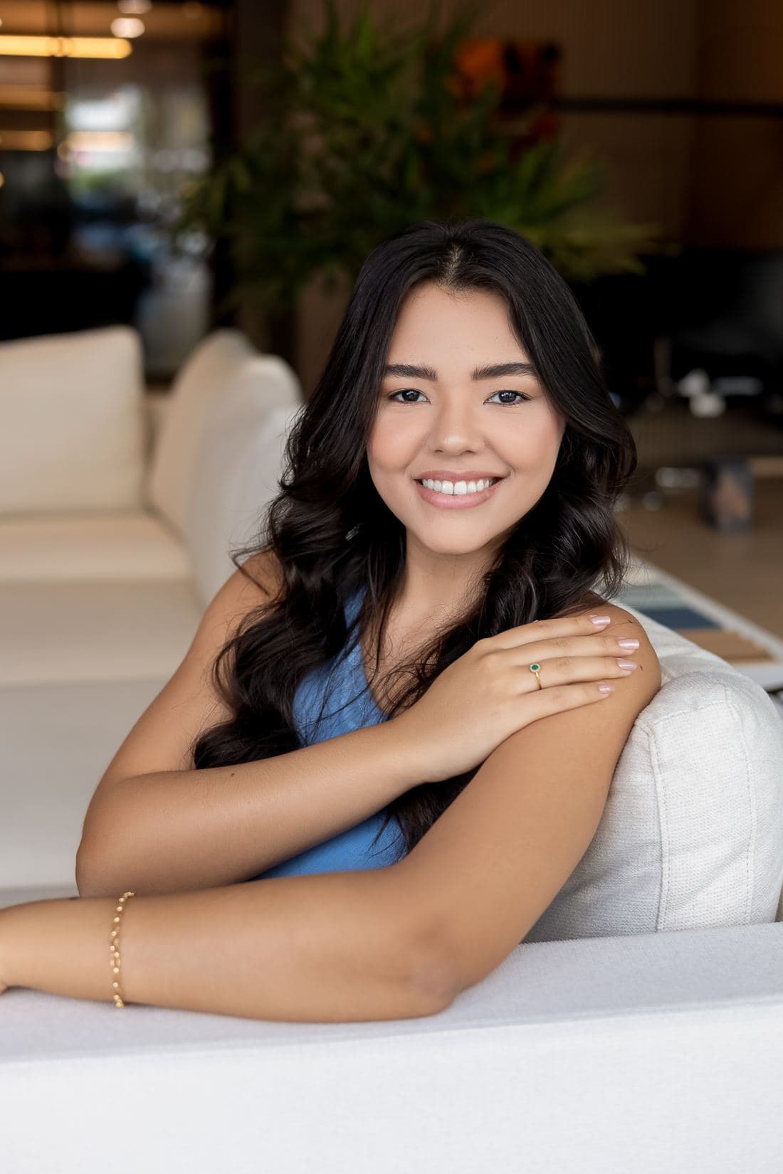 Amanda Morais sorrindo, apoiada no encosto de um sofá claro